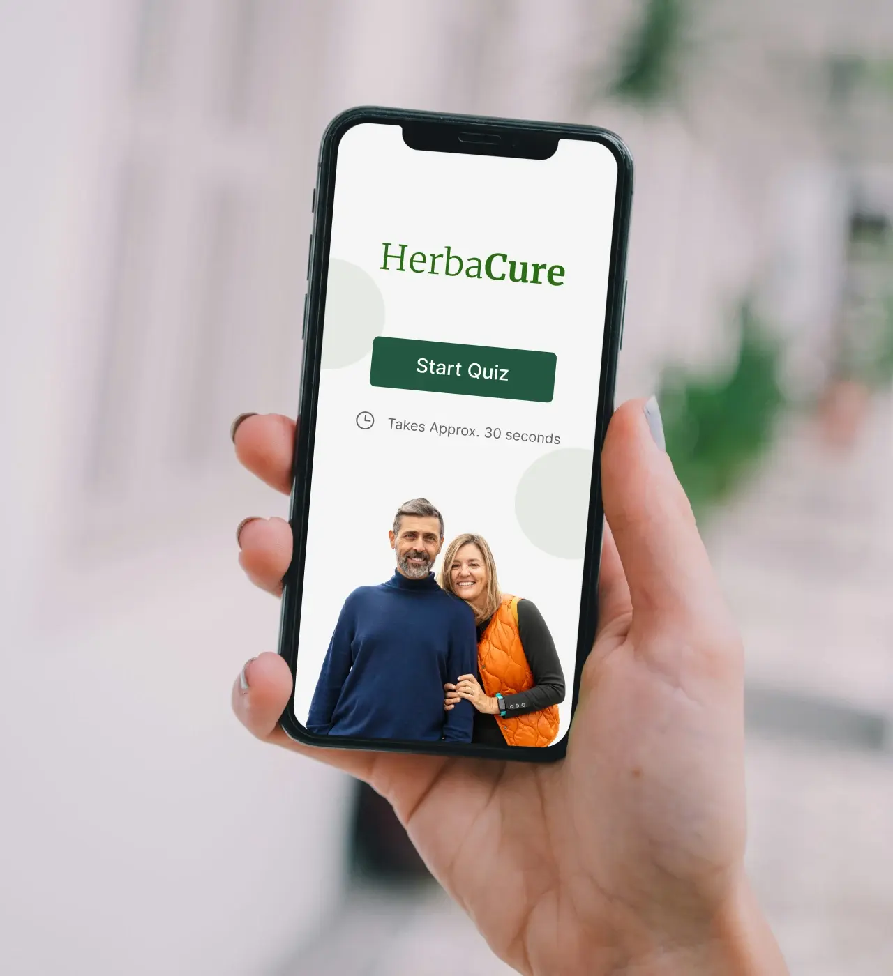 Hand holding a smartphone displaying the HerbaCure app screen, with a "Start Quiz" button and an image of a smiling couple.